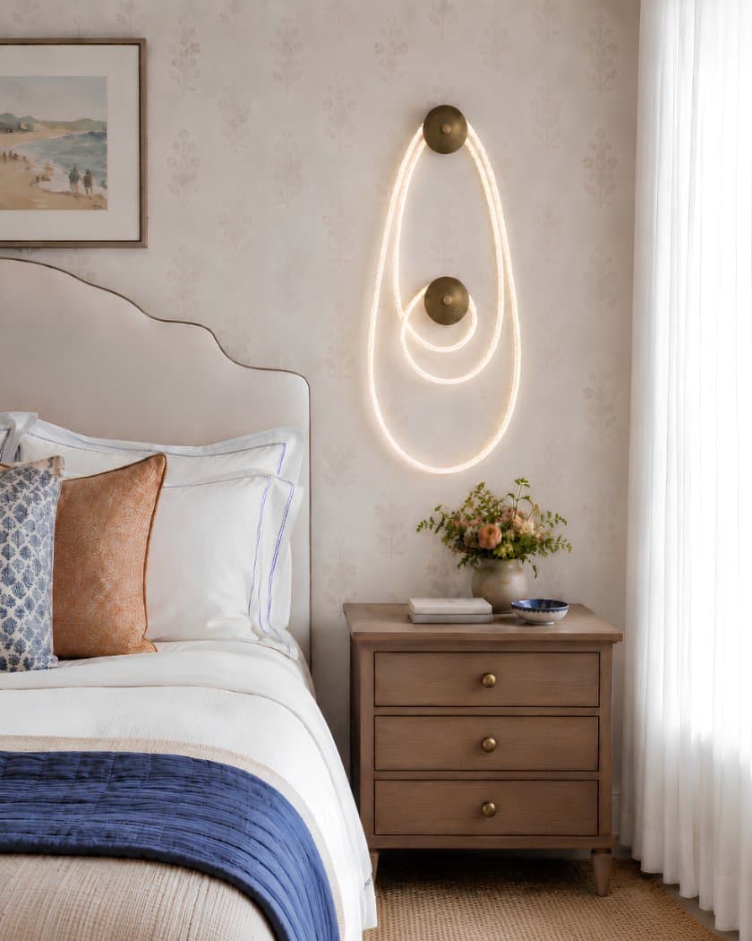 Selene wall fixture in aged brass, with illuminated cord looped between two circular wall canopies beside a bed