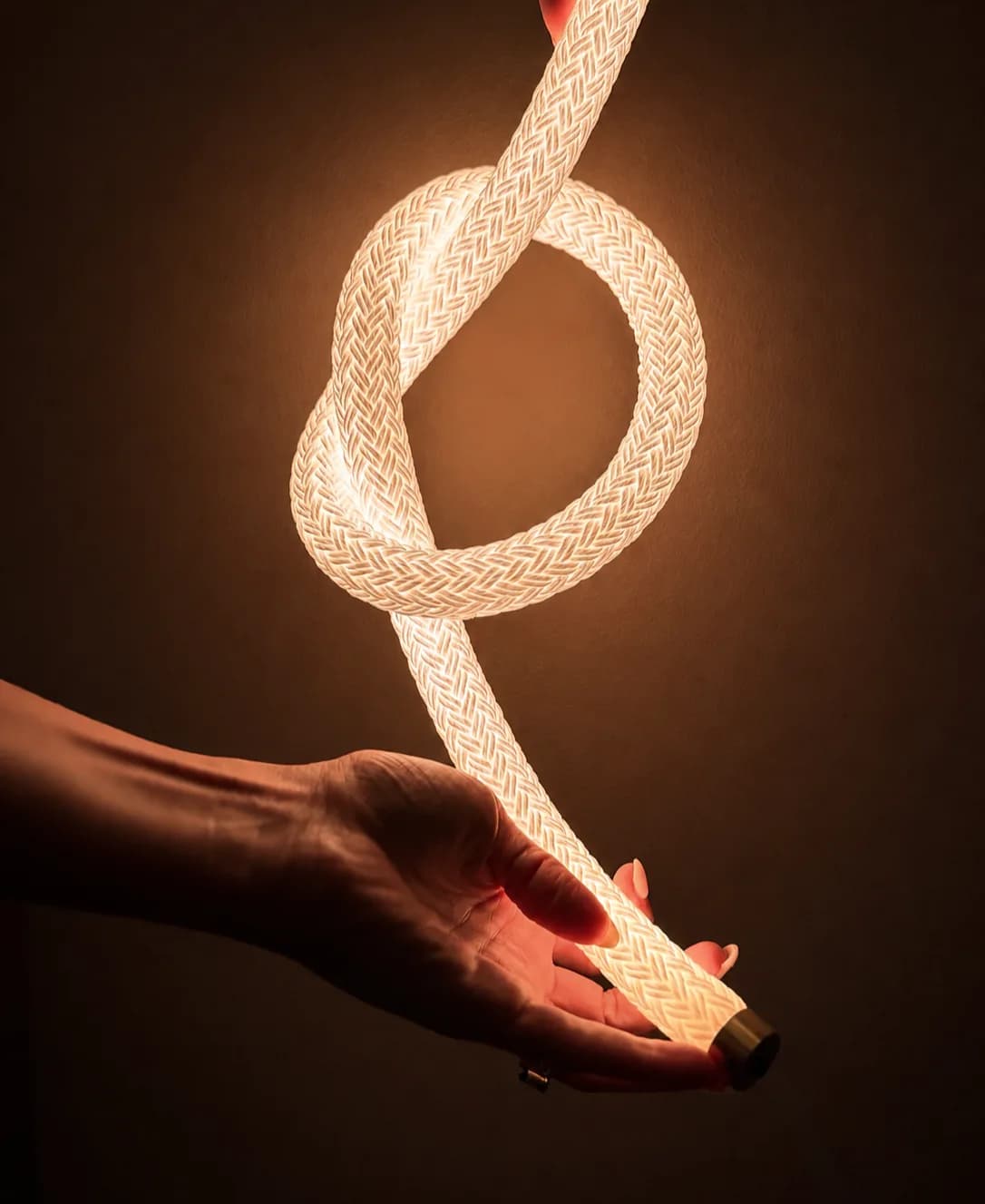 Hands holding a knotted length of illuminated braided cord with a brass end cap