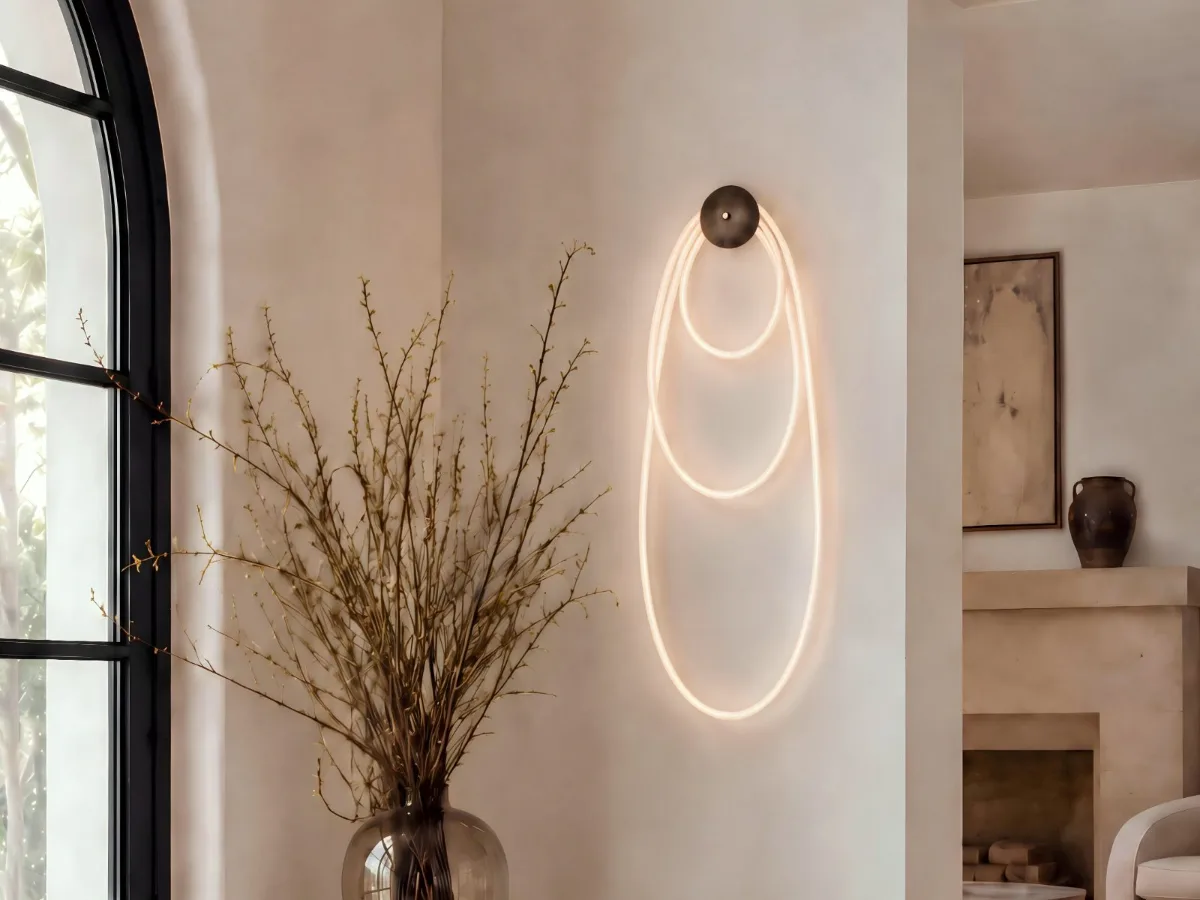 Selene wall fixture with illuminated cord looped in three nested ovals from a single dome canopy, on a plaster wall beside an arched window