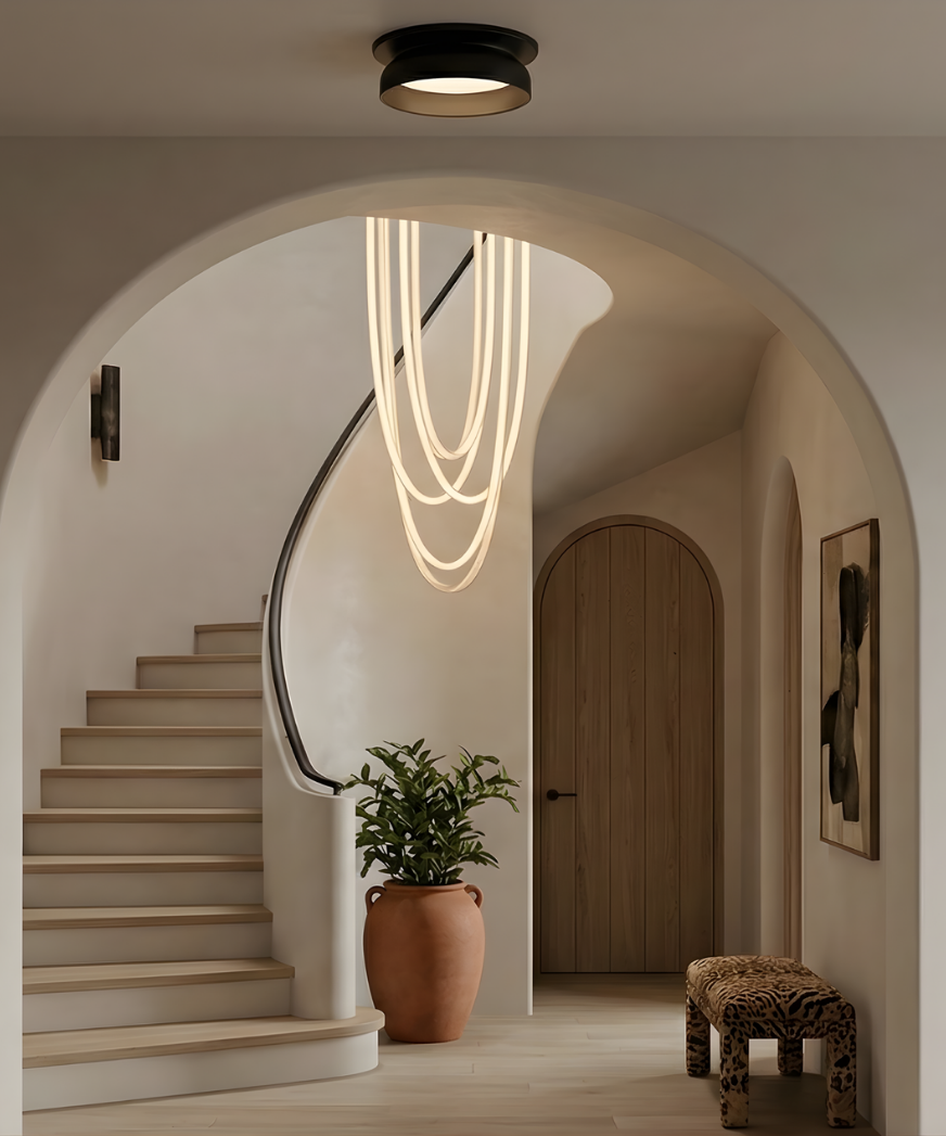 Modern entryway with curved plaster arch and staircase, featuring a sculptural looping pendant light composed of continuous illuminated rope suspended from the ceiling.