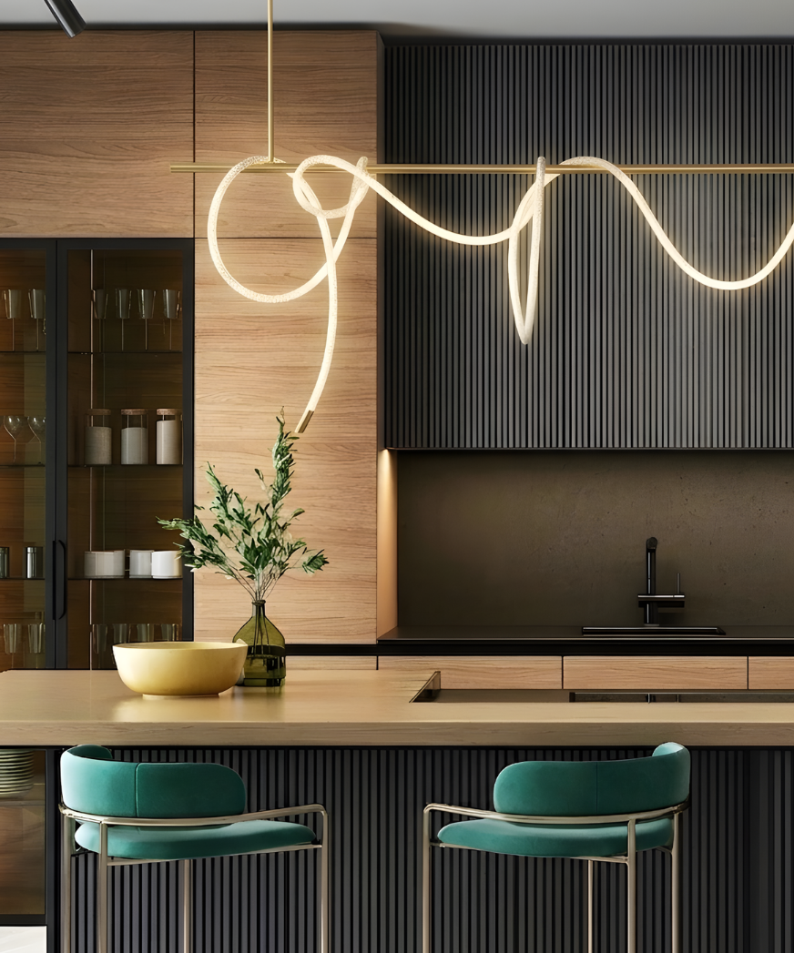 Contemporary kitchen with wood cabinetry and dark ribbed island, featuring a linear brass pendant with draped illuminated rope forming a fluid, wave-like shape above the counter.